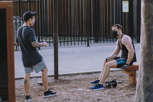 Two men wearing face masks while interacting outdoors